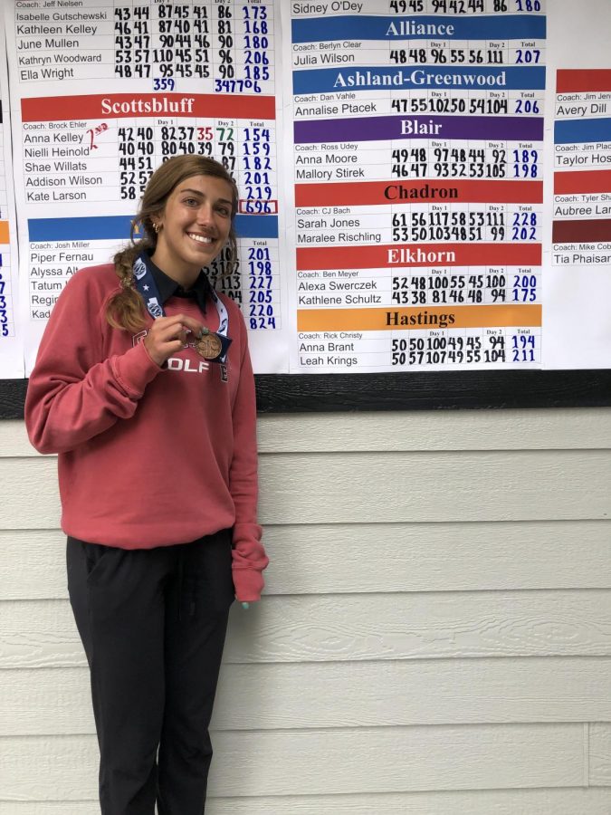 Katie Schultz poses with her metal and her score on the scoreboard at state golf.