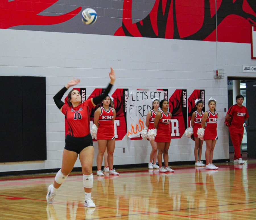 Avery Hoegh serves in volleyball game against Mercy, with support from the Antler cheerleaders.
