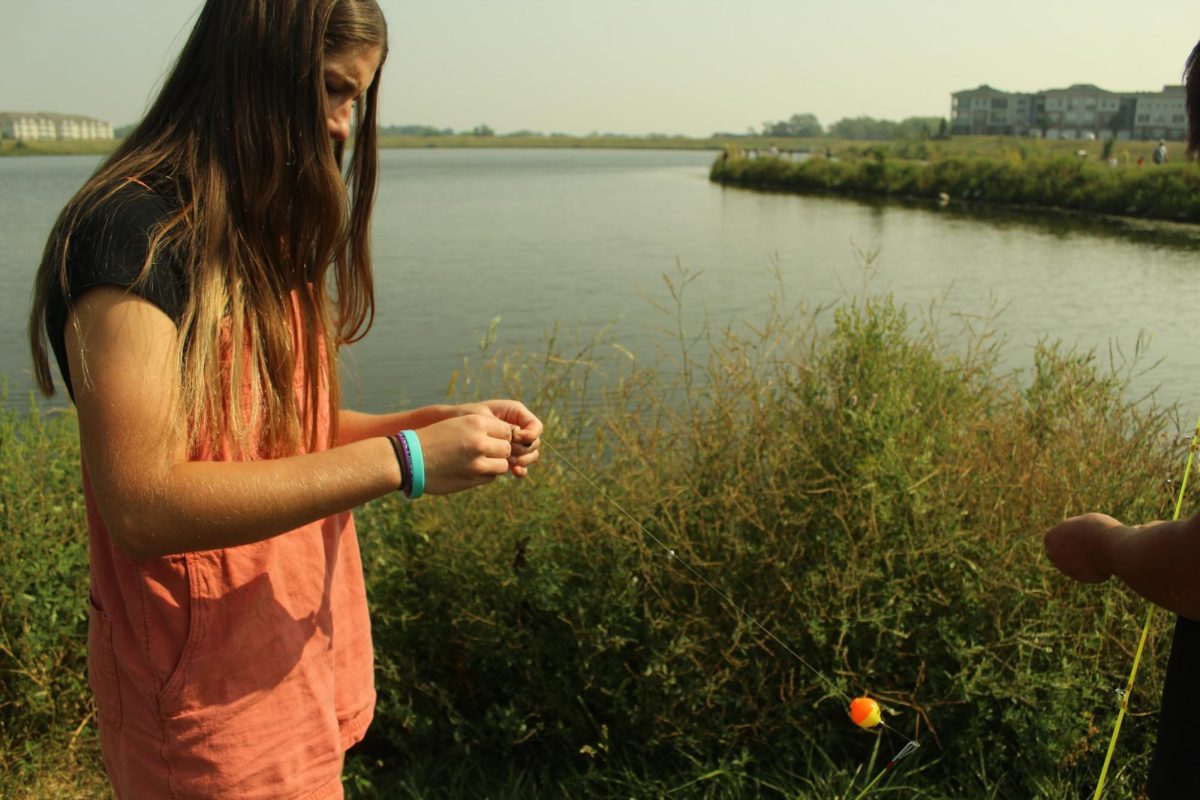 Senior Claire Nuismer attaching a worm to a hook during lifetime fishing field trip. 