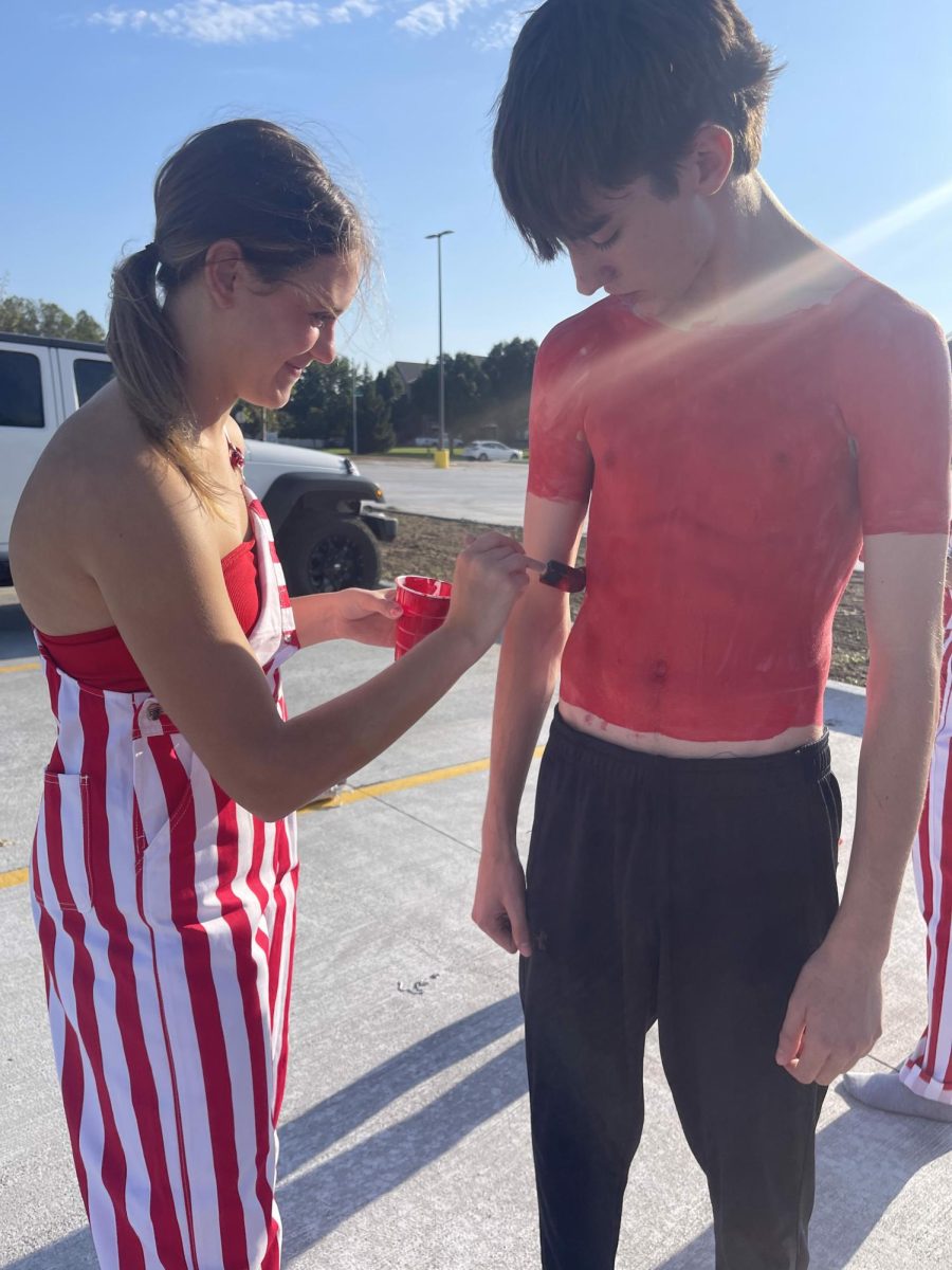 Senior Emmy Mcelhose painting senior Jacob Leyda before Gatorade scrimmage. Mcelhose does four different coats just to make sure the red is showing on Leyda's skin.