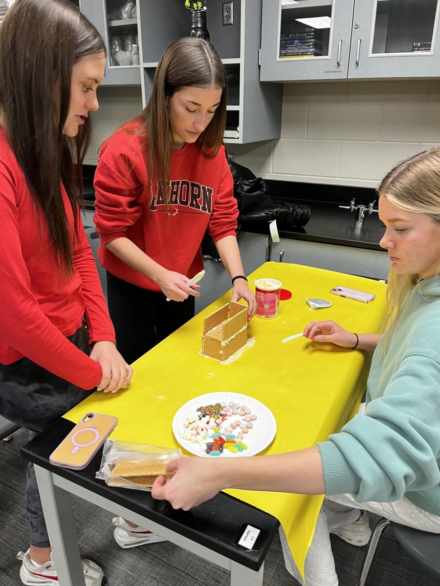 Seniors Becca Leise, Ava McCaslin, and Emmy McElhose build a beachy gingerbread house. The house was inspired by science teacher, Connie Bang's story about her Hawaii adventure.