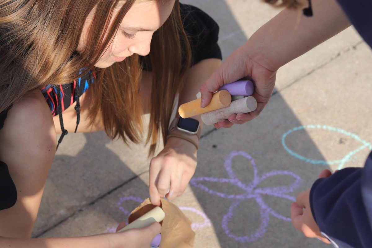 Sophomore Abby Haug gathers chalk after completing her chalk message on the sidewalk in front of the school. 
